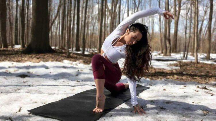 Woman doing yoga on a black mat in a snow-covered forest