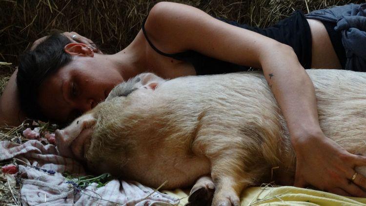 Woman lying down next to a pig with her arm around it
