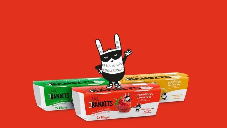cartoon character with black eyemask standing on top of red and white colored yoghurt packed box with green and yellow colored packed yoghurt boxes and red background