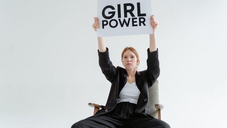 woman sitting on a chair holding a placard that says ‘girl power’