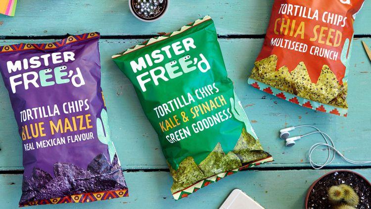 red, purple and green coloured packets of Mister Free'd chips lying on a terquise blue table.