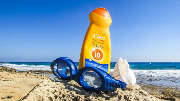 A yellow bottle of Cien sunscreen on a beach with a pair of swimming goggles