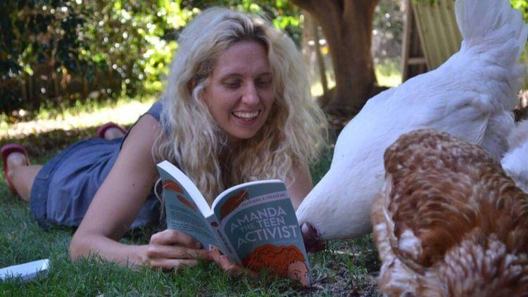Smiling women holding open a book in front of some chickens