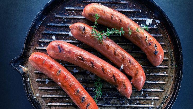A pan with four sausages on, they have been sprinkled with salt and garnished