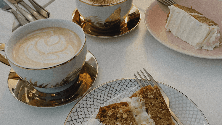 Cups of coffee on a table with cutlery and a piece of cake on a plate