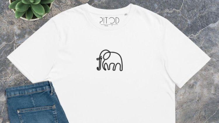 white graphic T-shirt with an elephant outline design next to a pait of folded jeans on a tiled floor