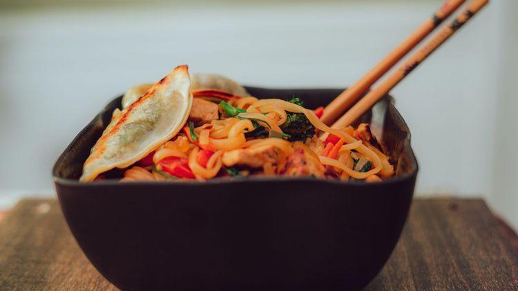 black bowl with noodles, dumplings and a pair of chopsticks poking out the top