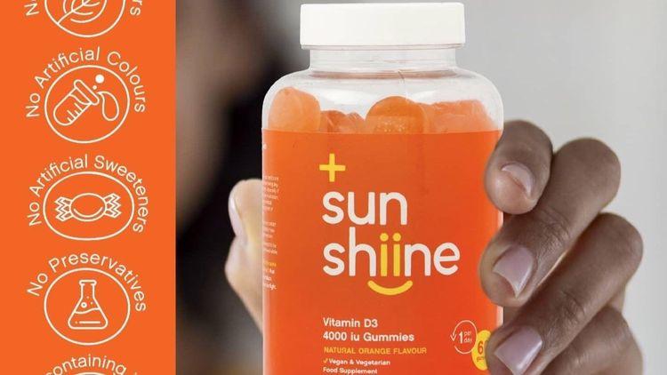 A hand holding an orange tub a tub of a vegan vitamin D supplement
