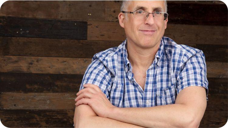 photo of a smiling man (Tim Barford,  Vegfest founder) in glasses and a chequered shirt