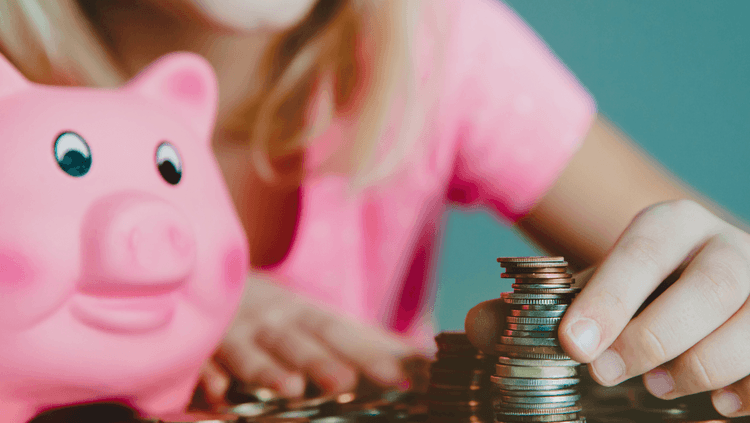 Young girl in a pink top counting piles of coins that have been taken out of her pink piggy bank next to her