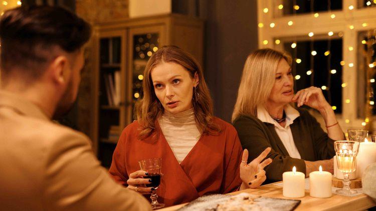 Disgruntled looking women chatting with men in a festive looking room with candles and lights 