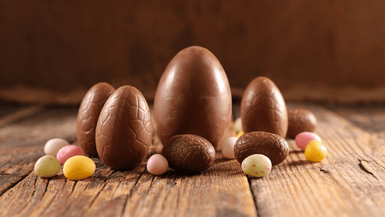 Multiple chocolate vegan Easter eggs in various sizes and colours on a wooden table 