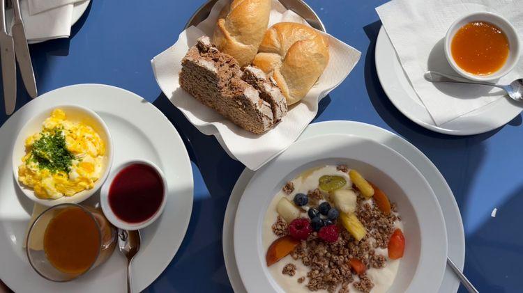 A spread of vegan brunch items: bread; granola with mixed fruit; jams etc. on a blue table cloth