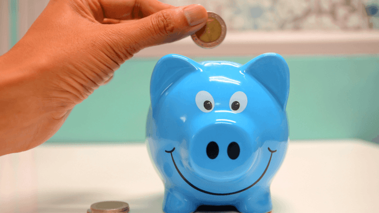 Hand putting a 20p into a smiling blue piggy bank 