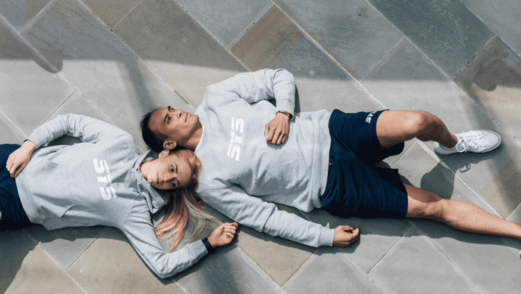 Man and women lying next to each other in the sun on some concrete both wearing the same outfit by SYS Sportswear (grey sweatshirt and black shorts)