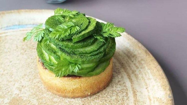 Vegan pastry with cucumber and greenery piled on top on a rustic plate