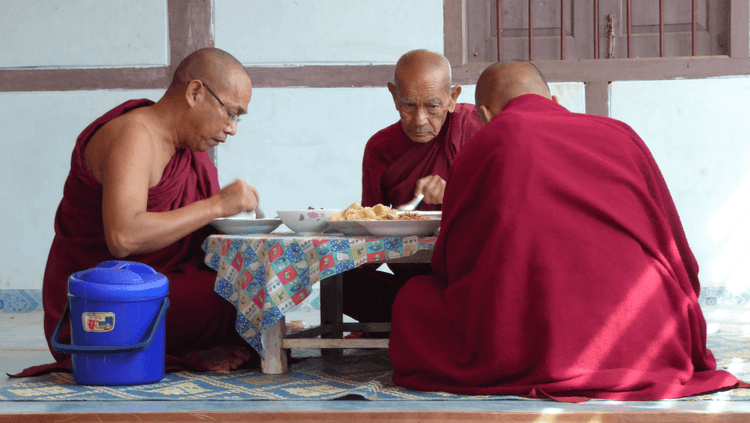 Three Buddhist monks in red robes eating a Buddhist diet together sat down around a table  
