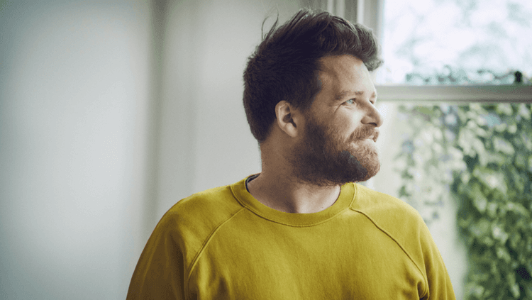 Smiling bearded man (Tom Hunt) looking into the distance in a yellow sweatshirt