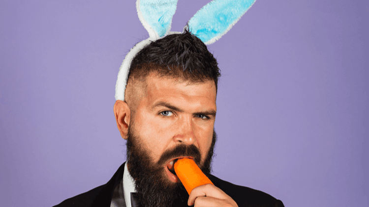 Bearded dark man with blue bunny ears on eating a carrot