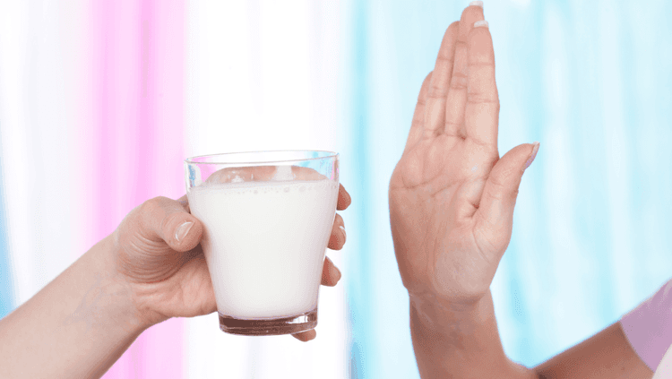 A glass of milk being handed to someone who has their hand raised to signal they don’t want the milk