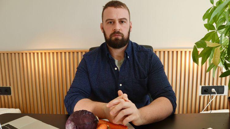 David Cleary sitting at a desk with his hands together with a plate with vegetables in front of him