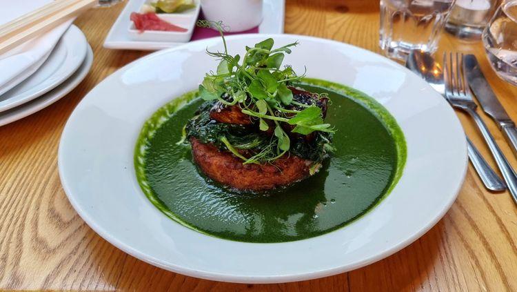 Potato rosti in a vibrant green sauce in a white bowl on a wooden table