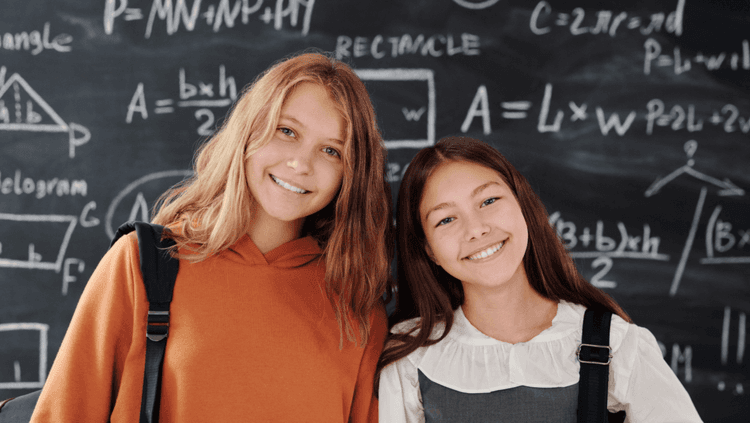 Two girls smiling in front of a blackboard 