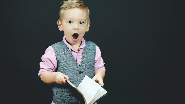 Young boy holding a book looking shocked with his mouth open