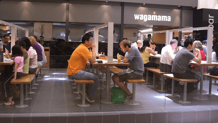 Individuals eating at Wagamama inside a food court 