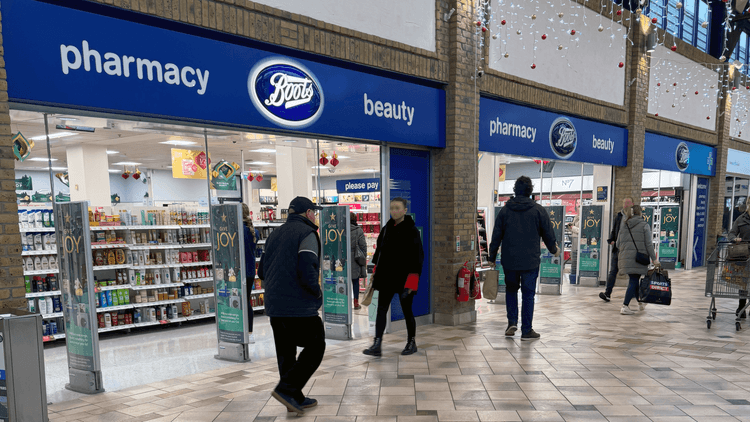 Boots storefront in a shopping centre with some people walking past it